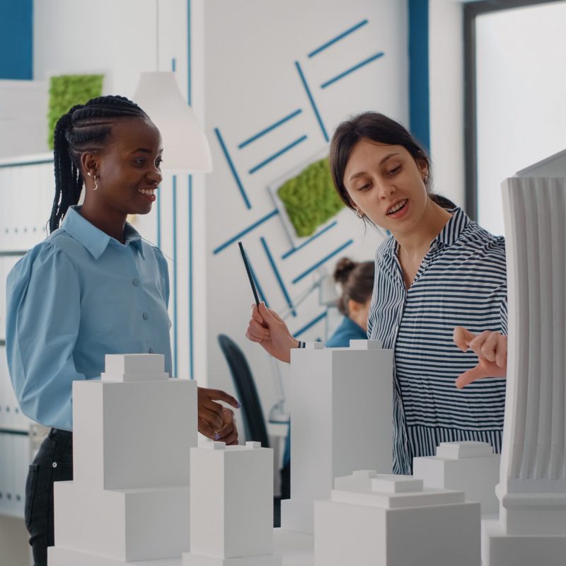 Architects giving highfive and celebrating urban project progress with building model. Colleagues doing teamwork on construction design and structure, using maquette in office.