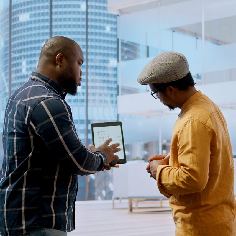Real estate broker and client negotiating a leasing contract for a high class modern office space, evaluating blueprints on tablet during office tour. Property investment opportunity. Camera A.